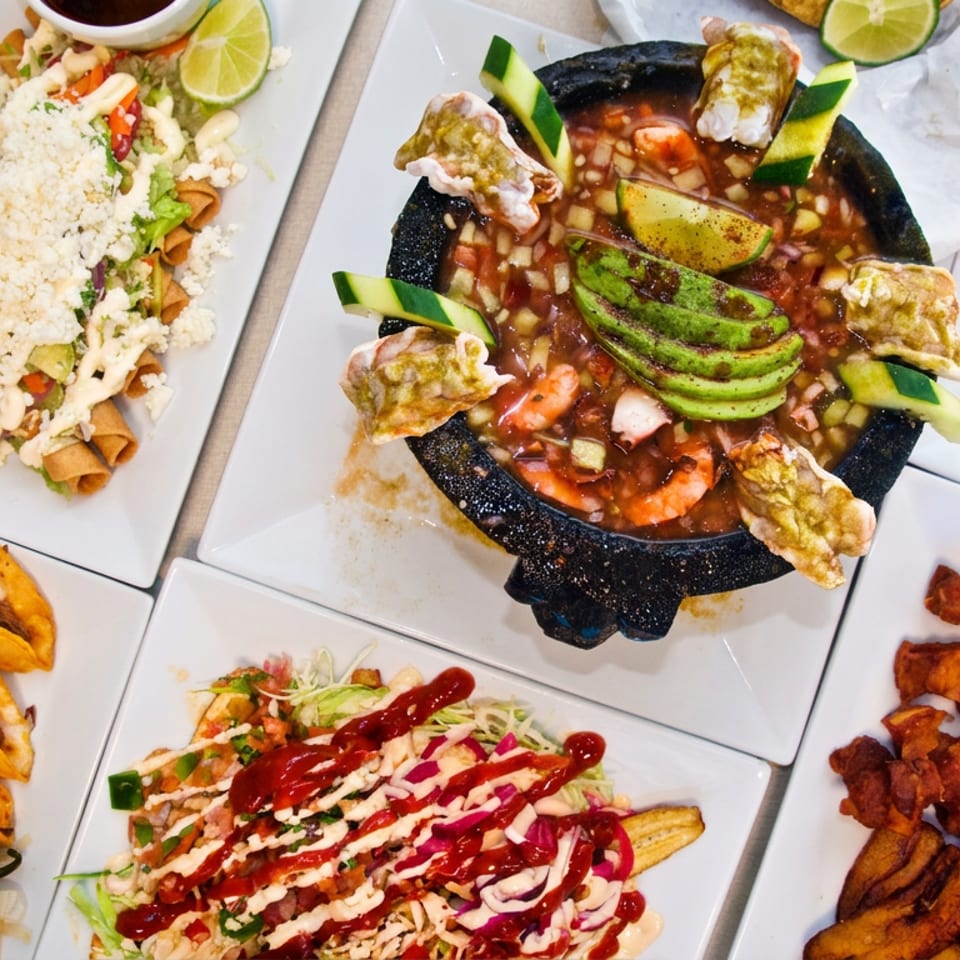 Overhead spread of Mexican dishes featuring tacos, shrimp ceviche, salads, grilled vegetables, rice, and colorful garnishes.